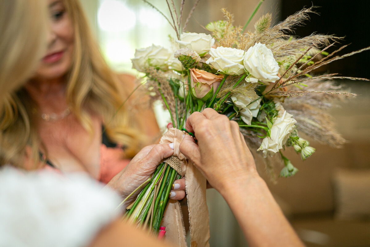 Close up shot of a lady tying ribbon to the bouquet for the vow renewal, the bouquet consists of white and soft pink roses and pampas grass.