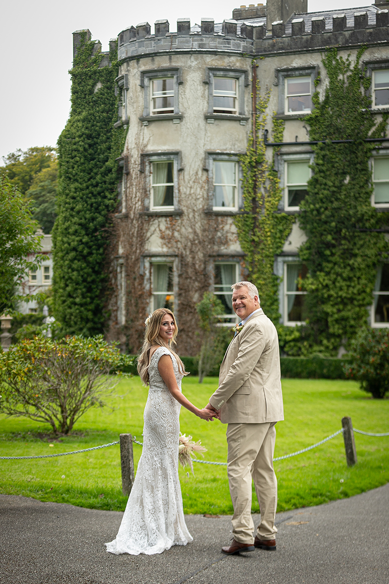 Husband and wife stand turning back to the camera in front of Ballyseede castle, Tralee.