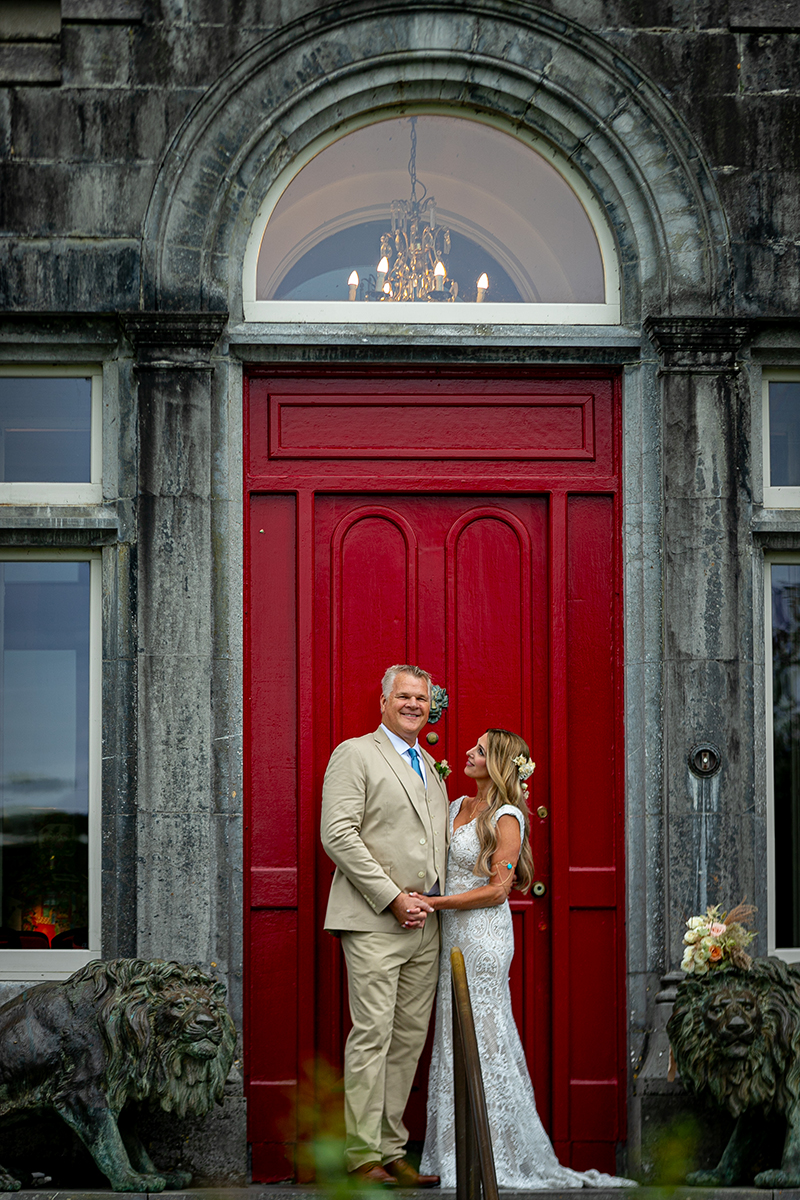Husband and wife standing in front of the red door of Ballyseede castle hotel, Tralee.
