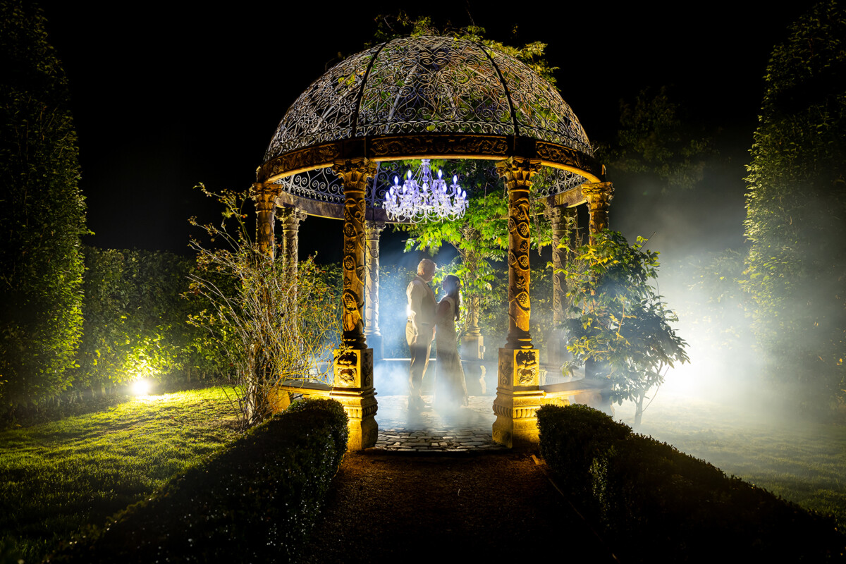 Nighttime shot of husband and wife standing in the centre of the stone gazebo at Ballyseede castle hotel.
